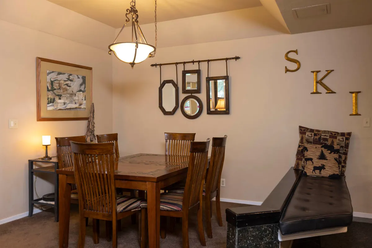 A warm, welcoming dining area featuring a sturdy wooden table, comfortable chairs, ski-themed wall decor, and a tasteful lighting fixture. The setting is perfect for family meals, game nights, and celebrating special occasions.