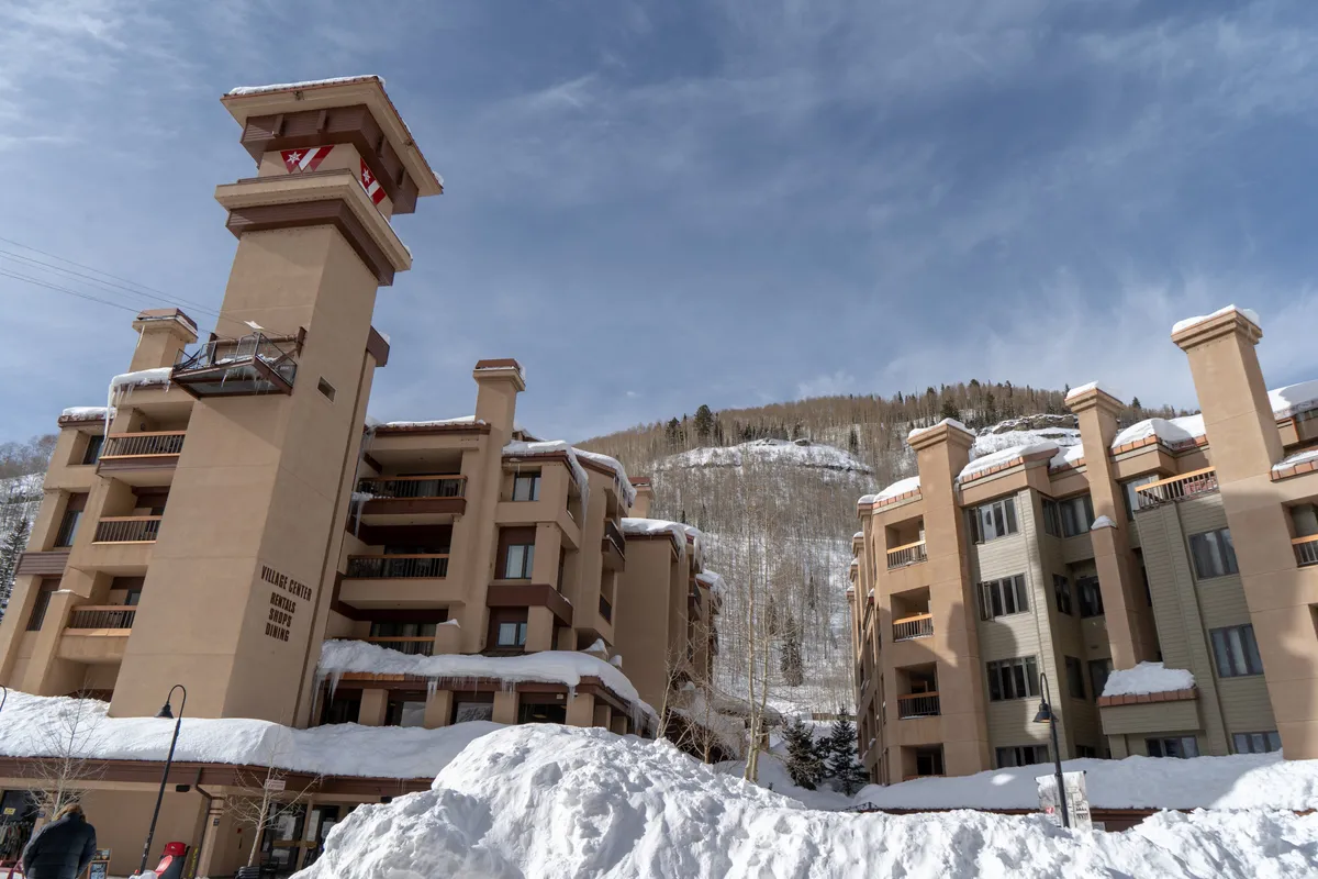 A striking exterior view featuring a tall architectural feature against a snow-covered landscape, framed by the surrounding towering mountains. The image evokes a sense of adventure and luxury, hinting at the nearby ski slopes and winter activities.