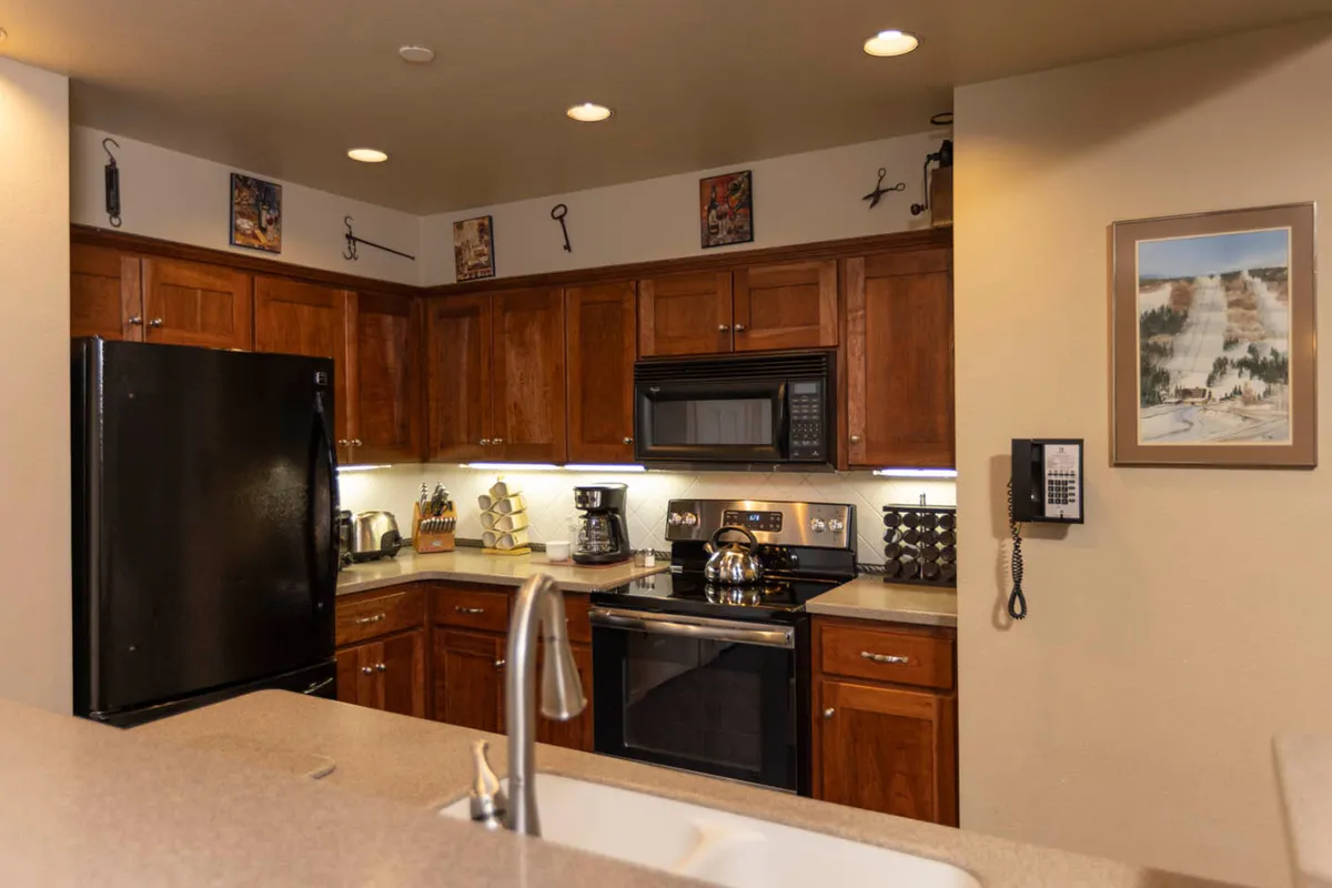 A cozy kitchen scene with a black refrigerator, stainless steel appliances, wooden cabinetry, and a central kitchen island. Decorative wall art adds a personal touch, and the space exudes warmth, ideal for family gatherings or intimate dinners.