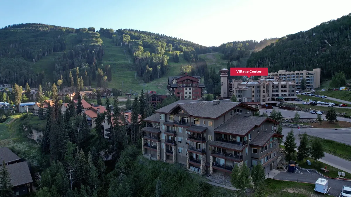 A broad view of the mountains and surrounding residential buildings, with trees and a parking area in the foreground. The scene speaks to the alpine setting and the village atmosphere, ideal for exploring and gathering with loved ones.