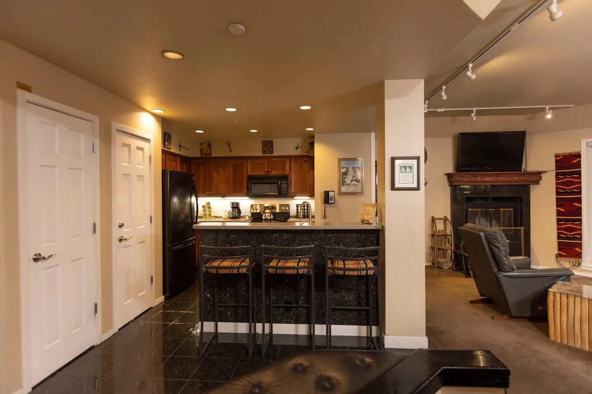 This image features the kitchen island with bar stools, complemented by sleek black appliances and a cozy seating area near a fireplace. The overall ambiance is warm and inviting, with plenty of space for cooking and socializing. The kitchen island is set up for shared meals or casual conversations while preparing food.