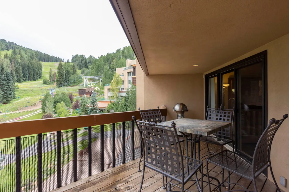 This image captures an outdoor dining area surrounded by lush trees with a clear view of the nearby mountain slope. The table is set for enjoying meals or drinks outdoors, and the peaceful mountain scenery forms a beautiful backdrop, suggesting relaxation and connection with nature.